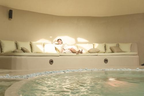 a woman sitting on a couch next to a swimming pool at Terme di Vulci Glamping & Spa in Canino