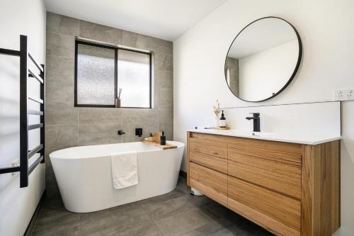 een badkamer met een bad, een wastafel en een spiegel bij Beach Walk on Alfred in Bridport