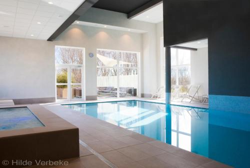 a large swimming pool with blue water in a building at Domein Westhoek Apartment in Oostduinkerke