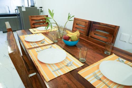 a wooden table with white plates and a bowl of fruit at Lime Tree Service Apartment - Near Artemis Hospital ,Gurgaon in Gurgaon