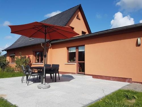 a table and chairs with a red umbrella in front of a house at Ruegen Fewo 111 in Drewoldke