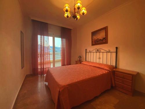 1 dormitorio con cama, ventana y lámpara de araña en Apartamento Coliseo Almuñecar, en Almuñécar