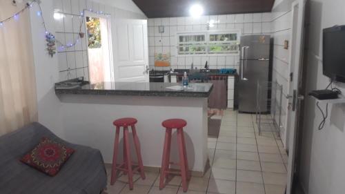 a kitchen with a counter and two red stools at Aconchego 3 dorms, piscina, churrasq em Condomínio Fechado in Boicucanga