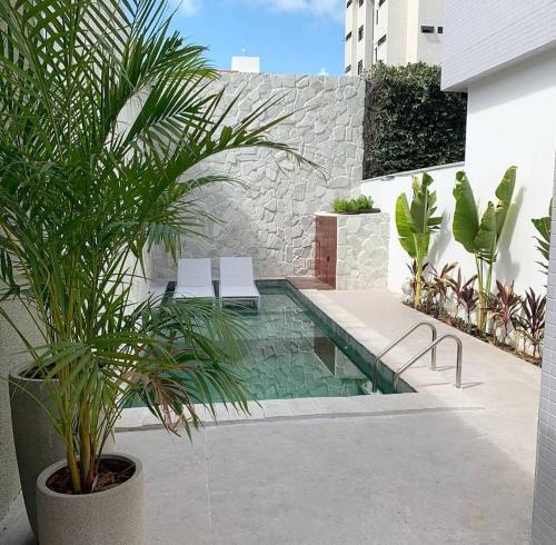 a swimming pool with two white chairs and plants at Flat Bauten Cabo branco AP301 in João Pessoa