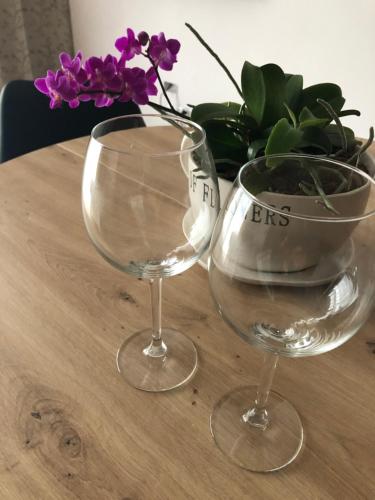 two wine glasses and a vase with purple flowers on a table at Apartament Chopina in Łomianki