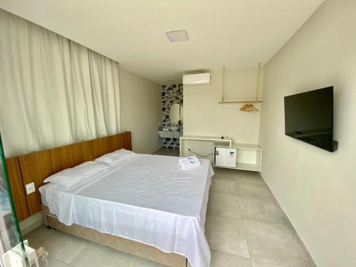 a bedroom with a white bed and a flat screen tv at Santo Mar Em São Miguel do gostoso in Touros