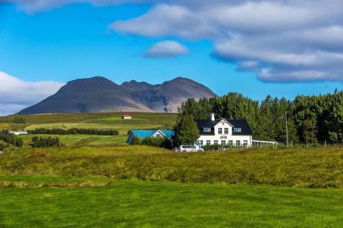 a house in a field with mountains in the background at Guesthouse Húsid in Hlíðarendi