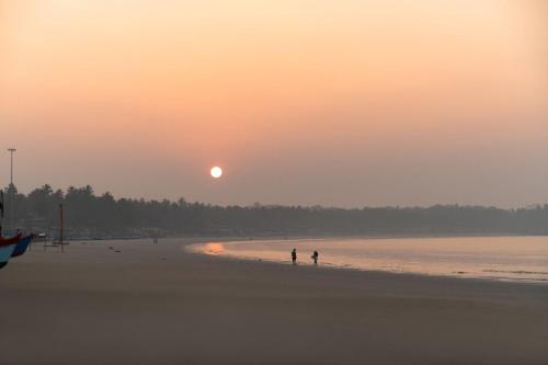 dwie osoby spacerujące po plaży o zachodzie słońca w obiekcie Oxygen Palolem w mieście Palolem