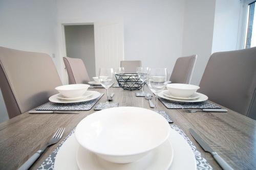einen Holztisch mit weißen Tellern und Weingläsern in der Unterkunft Herbert House by StayStaycations in Treorky