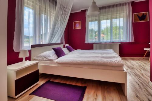 a bedroom with a bed with purple walls and windows at Vincze Villa Vendégház in Bükkszék