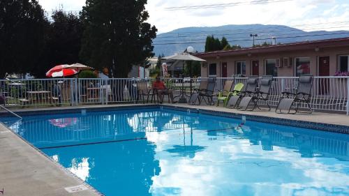 a blue swimming pool with chairs and tables and a building at Swiss Sunset Inn in Penticton