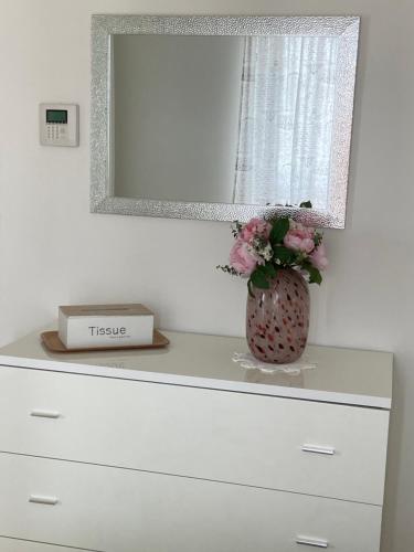 a dresser with a mirror and a vase with flowers at AGM Suite Rome Airport FCO - Attico Parco Leonardo in Fiumicino