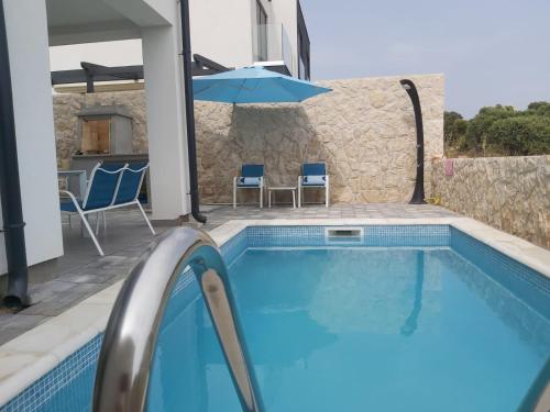 a swimming pool with a blue umbrella and chairs at PALMandre (Pag Apartment Luxurious) in Mandre