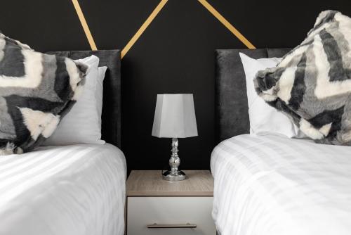 two beds with white sheets and a lamp on a night stand at City Centre Studio 4 with Kitchenette, Free Wifi and Smart TV by Yoko Property in Middlesbrough