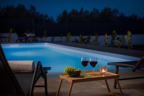 two glasses of wine on a table next to a swimming pool at Villa Millennium in Jezera