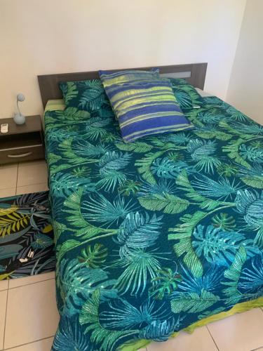 1 cama con edredón azul y verde y almohada en Villa Karata Appartement T3 avec Spa et vue sur mer BAILLIF Basse-Terre, en Baillif
