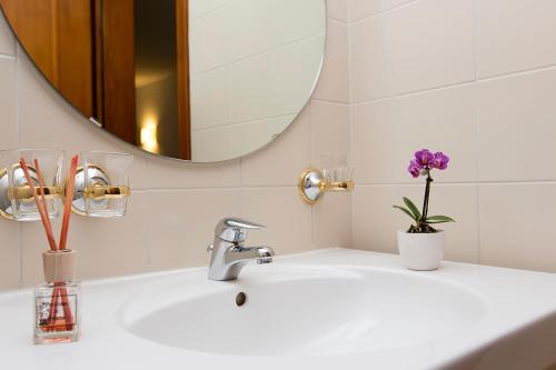 een wastafel in de badkamer met een spiegel en een vaas met paarse bloemen bij Hotel Ristorante Walser in Bosco Gurin