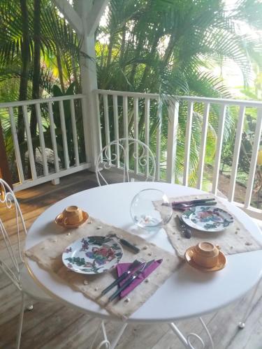 a white table with plates and utensils on a porch at Chambre d'hôte et Loft dans maison de charme piscine à débordement La Villa Gialla in Schœlcher