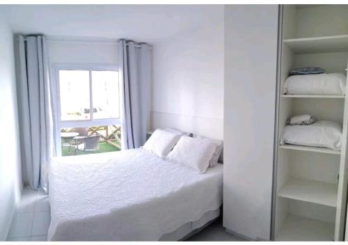 a white bedroom with a bed and a window at Flat Terreo Muro Alto Condomínio Clube com Sala Reversível para segundo quarto in Porto De Galinhas