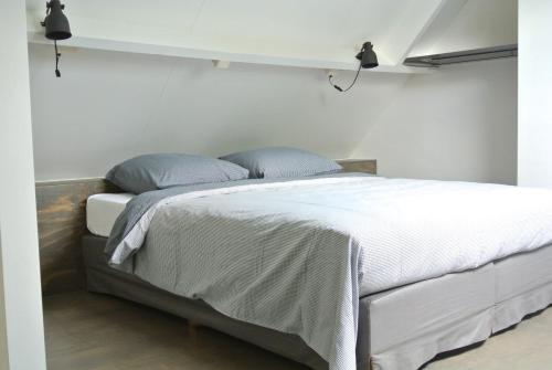 1 dormitorio con 1 cama con sábanas blancas y almohadas azules en De Heerlykheid, en Nuenen