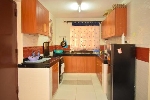 a kitchen with wooden cabinets and a black refrigerator at Wawa Lifestyle Regency one bedroom Apartment in Nairobi