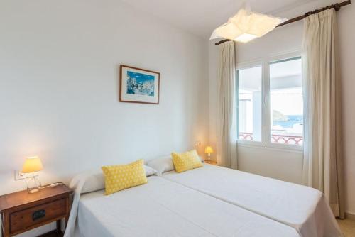 a white bedroom with a bed and a window at Apartamento Sa Mesquida 11 in Cala Llonga