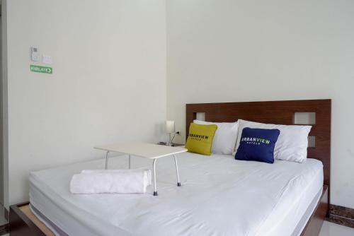 a white bed with two pillows and a table on it at Urbanview Hotel Syariah Casa Azmya Yogyakarta by RedDoorz in Kejayan