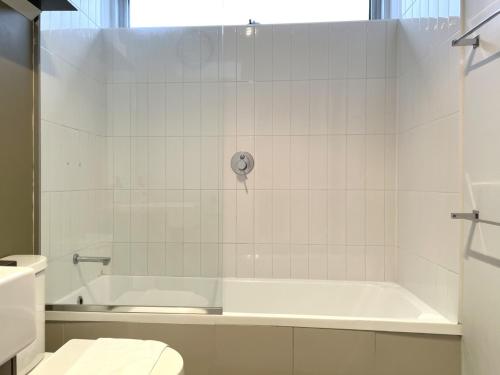 a white bathroom with a tub and a toilet at Readyset Apartments at Verve in Melbourne