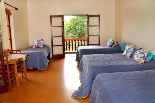 a room with three beds and a balcony with a door at Pousada do Sitio in São Bento do Sapucaí