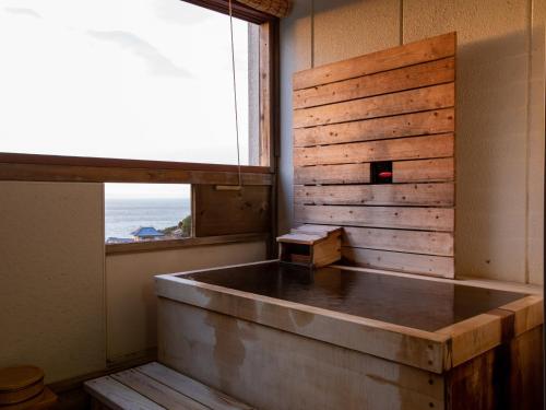 a room with a bath tub with a window at Hotel Tenzankaku Kaiyutei in Shirahama