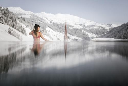 a woman standing on a lake with mountains in the background at Aktiv- & Wellnesshotel Bergfried in Tux