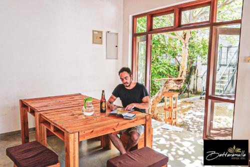 a man sitting at a wooden table with a bottle of beer at Battaramulla Boutique Villa in Sri Jayewardenepura Kotte