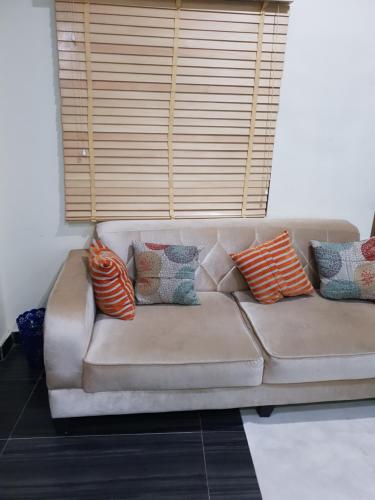 a brown couch with pillows sitting under a window at NESTAPARTMENTS , Orchid Road , VAN DANIEL'S STREET, LEKKI , Ensuite ,WiFi in Lagos