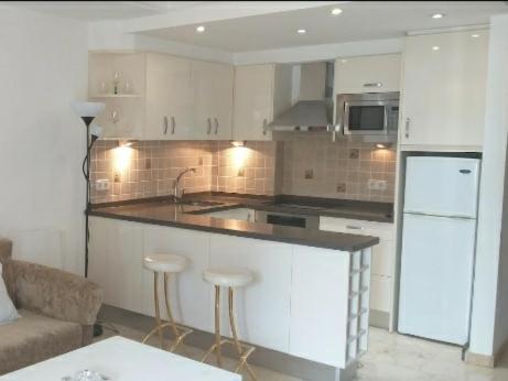 uma cozinha com armários brancos e um balcão com bancos de bar em Apartamento en la milla de oro, a 100m de la playa em Marbella