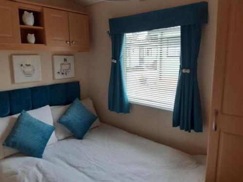 a bedroom with a bed with blue curtains and a window at 24 The Beeches Caravan Park in Gilcrux