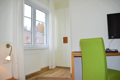 a green chair in a room with a desk and a television at Hotel Lindenallee in Lindau