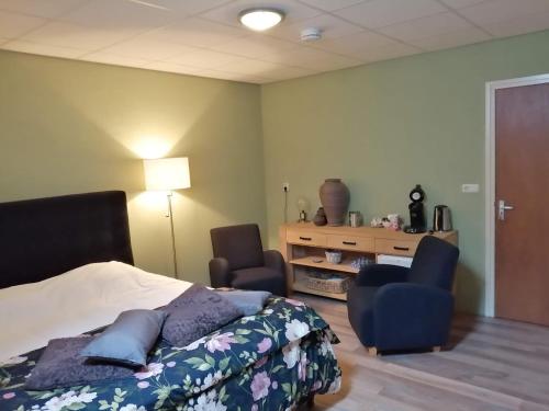 a bedroom with a bed and two chairs and a desk at De Kapschuur in Stadskanaal
