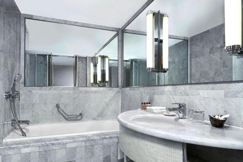 a bathroom with a tub and a sink and mirrors at Sheraton Paris Charles de Gaulle Airport Hotel in Roissy-en-France