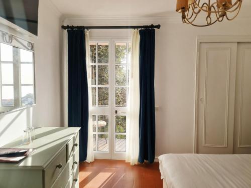 a bedroom with a bed and a window with blue curtains at Villa Alto Boutique Hotel in Ponta do Sol