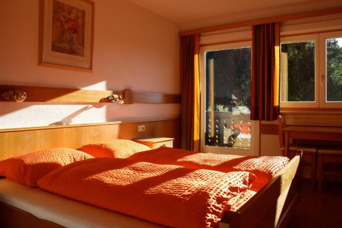 1 dormitorio con cama de color naranja y ventana en Pension Haus Maria, en Ramsau am Dachstein