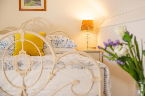 a white bed with a yellow pillow and a vase of flowers at Higher Weddicott Barn Holiday Cottage - Self Catering in Chagford