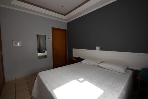 a bedroom with a white bed and a mirror at HOTEL ABAPORU in Adamantina