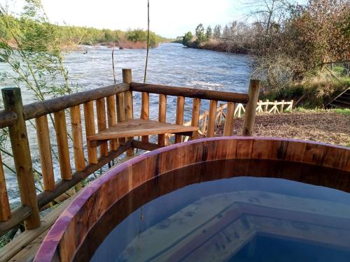 a wooden deck with a bench and a table next to a river at Casa del rio in Radal