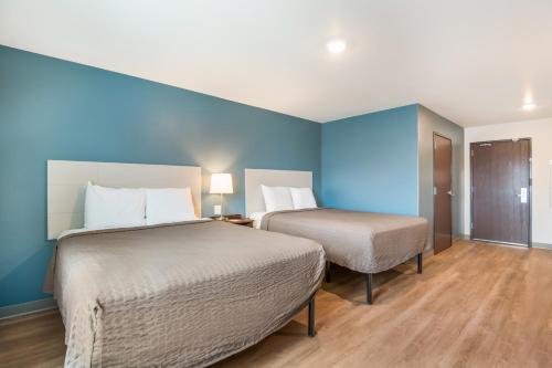 two beds in a room with blue walls and wooden floors at WoodSpring Suites Colorado Springs North - Air Force Academy in Colorado Springs