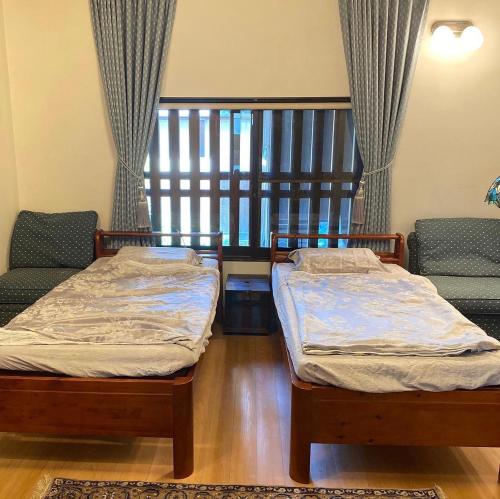 2 camas individuales en una habitación con ventana en 古民家民泊かえるて, en Kashihara