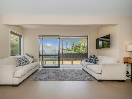 a living room with two couches and a sliding glass door at Seas the Day - Matarangi Holiday Home in Matarangi