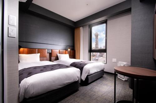 a hotel room with two beds and a table and a window at Hiyori Hotel Osaka Shinsekai in Osaka