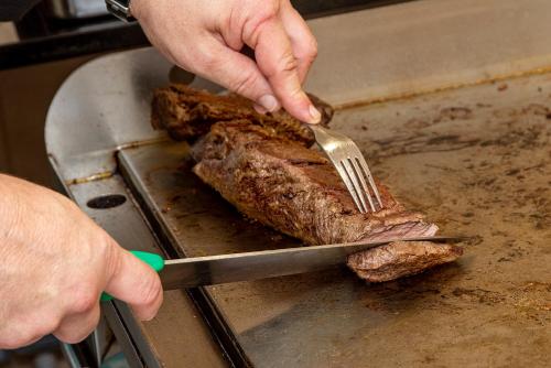 a person cutting a piece of meat with a fork at Hotel Biniamar in Cala Millor