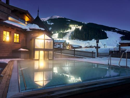 a swimming pool in front of a house with a mountain at Hotel Hasenauer in Saalbach Hinterglemm