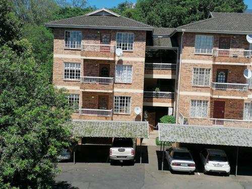 ein Apartmenthaus mit Autos auf einem Parkplatz in der Unterkunft ALL SAINTS ON ROBERTS in Pietermaritzburg